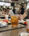 A clear glass pitcher filled with iced cola on a fast-food restaurant table, surrounded by a burger, fries, and drink cups, with a person's hand holding the pitcher, Commercial Polypropylene Beverage Pitcher Set, 1.5 Liter Clear Plastic Water Jug Bulk, Shatterproof Catering Pitcher Pack of 6, Hotel Buffet Plastic Drink Jugs, Unbreakable Restaurant Water Pitcher, Fluted Plastic Beverage Pitcher, Commercial Grade Clear Iced Tea Jug, 1.5L Plastic Pitchers Set of 6, Outdoor Catering Drinkware Bulk