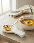 A white marble soup spoon rest holding a gold spoon with a daisy handle, styled on a wooden table next to a bowl of soup, Gold Stainless Steel Soup Ladle, Sunflower Decorative Ladle Set, 11 Inch Round Gold Serving Ladle, Set of 3 Gold Soup Spoons, Set of 5 Buffet Serving Ladles, Floral Enamel Handle Kitchen Utensils, Luxury Punch Bowl Ladle Gold, Gold Tableware Serving Utensils, Decorative Gravy Ladle Set, High End Kitchen Entertaining Accessories