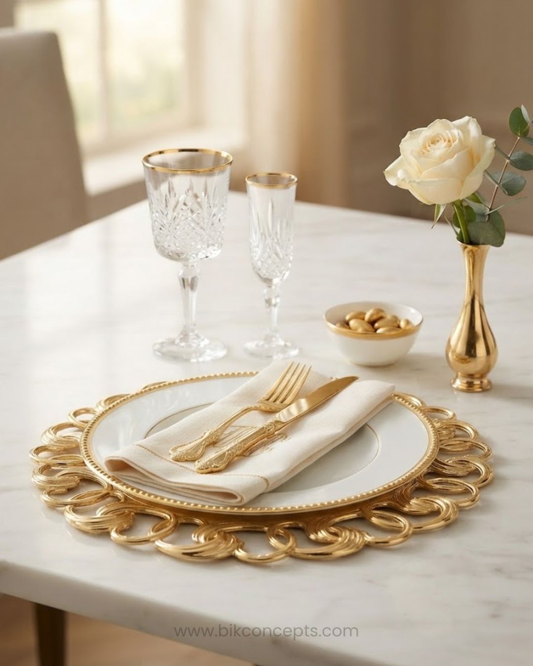 A styled table setting with a gold-plated charger plate, white dinner plate, cream napkin, gold cutlery, two crystal wine glasses with gold rims, a small bowl of chocolates, and a gold vase holding a white rose on a white marble table, Gold Charger Plates Set of 6, Interlocking Loop Plastic Charger Plates, 13 Inch Round Service Plates, Luxury Wedding Table Decor US, Catering Charger Plates Bulk, Openwork Chain Link Underplates, Gold Metallic Place Setting Base Plates, Modern Event Decor Charger Plates, Whol