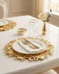 An elegant dining table setting featuring a gold-plated ornate charger plate with a white dinner plate, white napkin, gold cutlery, a clear crystal goblet, a small gold vase with a white rose, and a matching gold and white charger plate in the background, Gold Charger Plates Set of 6, Royal Crest Plastic Charger Plates, 13 Inch Round Service Plates, Luxury Wedding Table Decor US, Catering Charger Plates Bulk, Ornate Gold Place Setting Underplates, Gilded Scrollwork Table Base Plates, Event Decor Charger