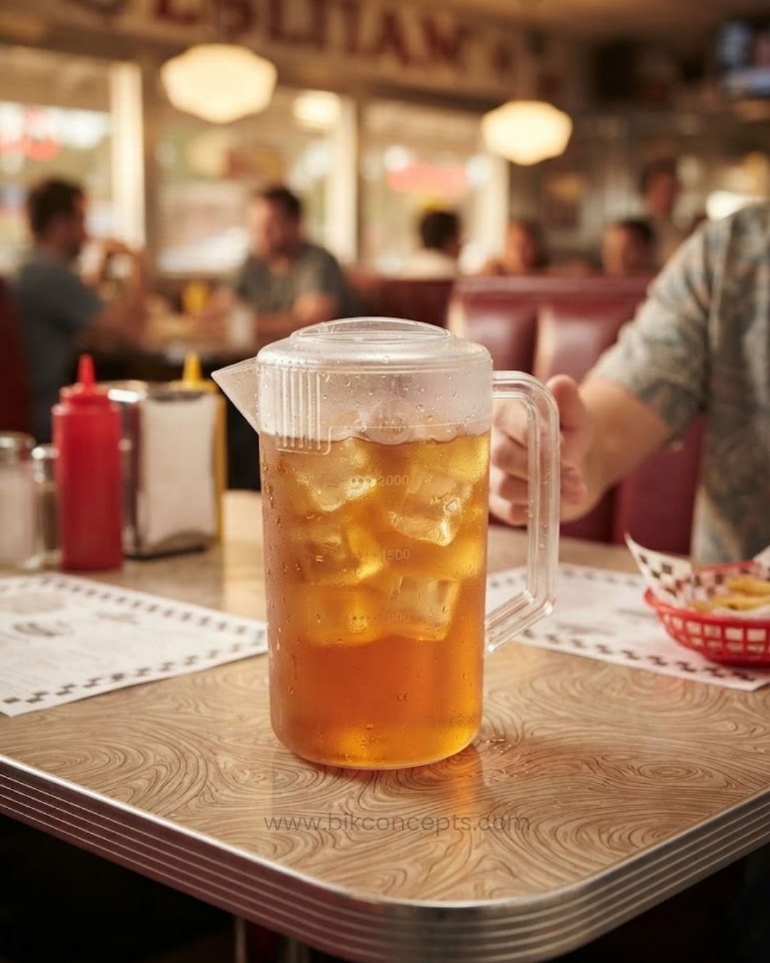 A clear plastic pitcher filled with iced tea and ice cubes sits on a diner-style table with a blurred restaurant background, Commercial Polypropylene Beverage Pitcher, 2.4 Liter Clear Plastic Water Jug, Shatterproof Catering Drink Pitcher, Hotel Buffet Beverage Service Pitcher, Measuring Plastic Pitcher with Lid, Restaurant Plastic Iced Tea Pitcher, Heavy Duty Commercial Plastic Jug, 2400ml Graduated Drink Pitcher, Outdoor Catering Plastic Pitcher, Clear Polypropylene Water Serving Jug