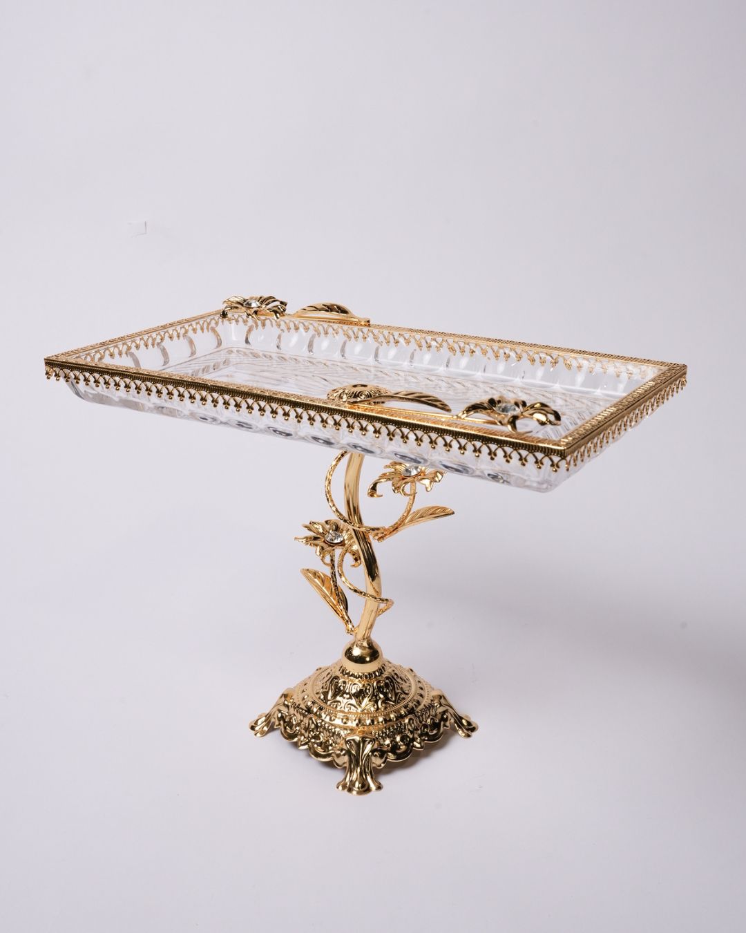 An ornate rectangular serving tray with a clear cut-glass or crystal top and an elaborate gold-tone metal base and trim, photographed against a plain light gray studio background.

Gold Pedestal Glass Serving Tray, Rectangular Glass Centerpiece Bowl, Vintage Gold Raised Dessert Platter, Floral Stem Footed Glass Tray, Luxury Table Centerpiece Dish, Gold Metal and Cut Glass Serving Tray, Decorative Coffee Table Platter, Crystal Gem Floral Serving Dish, High-End Appetizer Display Platter, Antique Style Gold Pe