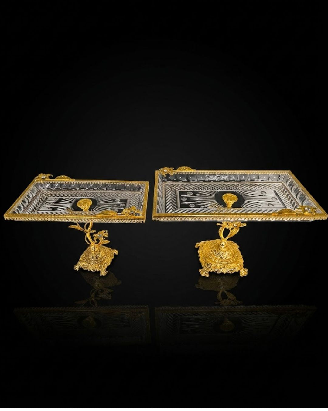 Two ornate rectangular gold and silver trays with sculpted gold pedestal bases, displayed on a reflective black background.