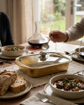 A rectangular gold-toned metal casserole dish with a glass lid and silver knob sits on a dining table set with bowls of stew, bread, wine glasses, and a decanter in a warm indoor setting.

Gold Stainless Steel Serving Platter, Covered Rectangular Food Server, Gold Chafing Dish Pan with Glass Lid, Luxury Catering Serving Tray, Metallic Buffet Server USA, Gold Lasagna Baking Dish with Lid, Decorative Food Storage Server, Covered Main Course Dish for Events, Gold Catering Pan for Weddings