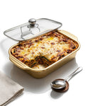 A rectangular gold-colored baking dish containing a baked lasagna, shown with a clear glass lid on a white background. A metal spoon rests on a small wooden stand beside the dish, and a folded beige cloth is visible in the lower left corner.

Gold Stainless Steel Serving Platter, Covered Rectangular Food Server, Gold Chafing Dish Pan with Glass Lid, Luxury Catering Serving Tray, Metallic Buffet Server USA, Gold Lasagna Baking Dish with Lid, Decorative Food Storage Server, Covered Main Course Dish for Events
