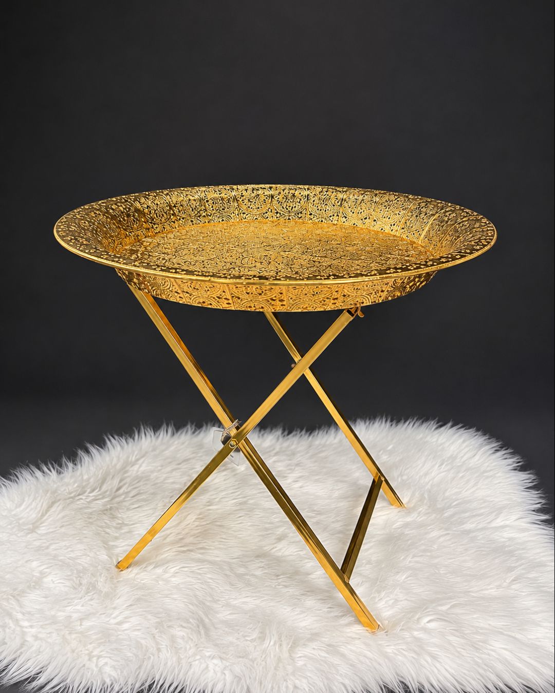 A round gold tray table with a textured, hammered-gold metal tray top and matching gold metal legs,Golden Round Serving Table, Embossed Metal Tray Table, Luxury Gold Accent Side Table, Moroccan Style Gold Tea Table, Designer Folding Drink Table USA, Filigree Metal End Table, Hollywood Regency Gold Furniture, Luxury Home Hosting Accessories, Decorative Metal Tray Table 20 Inch, High End Gold Bar Cart Alternative