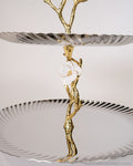 A two-tiered serving stand with a sculptural design, featuring a gold branch-like top and a central figure holding a white flower, 2 Tier Stainless Steel Platter, Luxury Tiered Dessert Stand, Jasmine Collection Serving Tray, High End Catering Platter USA, Silver Tiered Pastry Stand, Botanical Metal Buffet Display, Gold and Silver Tiered Tray, Designer Afternoon Tea Stand, Luxury Wedding Food Display, Decorative 2 Tier Metal Server