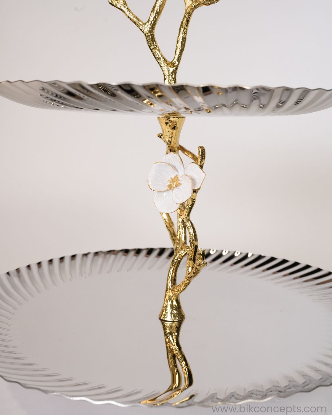 A two-tiered serving stand with a sculptural design, featuring a gold branch-like top and a central figure holding a white flower, 2 Tier Stainless Steel Platter, Luxury Tiered Dessert Stand, Jasmine Collection Serving Tray, High End Catering Platter USA, Silver Tiered Pastry Stand, Botanical Metal Buffet Display, Gold and Silver Tiered Tray, Designer Afternoon Tea Stand, Luxury Wedding Food Display, Decorative 2 Tier Metal Server