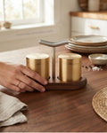 A close-up of a wooden salt and pepper shaker stand with two gold cylindrical containers and a brushed metal handle, Brushed Gold Stainless Steel Seasoning Set, Modern Salt and Pepper Shaker Set with Wood Base, Commercial Hotel Tabletop Seasoning Set, Luxury Catering Salt and Pepper Caddy, Gold Stainless Steel Spice Shaker Set, Tabletop Seasoning Cruet Set with Handle, Decorative Restaurant Salt and Pepper Dispenser, Stainless Steel Condiment Set with Wooden Tray, Gold Spice Shaker Set for Fine Dining, Comp