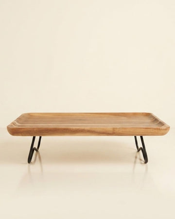 A rectangular wooden serving tray with a natural wood grain top and black metal hairpin legs, Elevated Wood Serving Tray, Raised Wooden Platter with Metal Legs, Wood and Metal Serving Board, Nature Enthusiast Home Decor, Rectangular Wood Table Riser, Solid Hardwood Buffet Platter, Rustic Modern Raised Serving Tray, Black Metal Base Wood Tray, Charcuterie Platter Riser, Biophilic Kitchen Serving Accessories