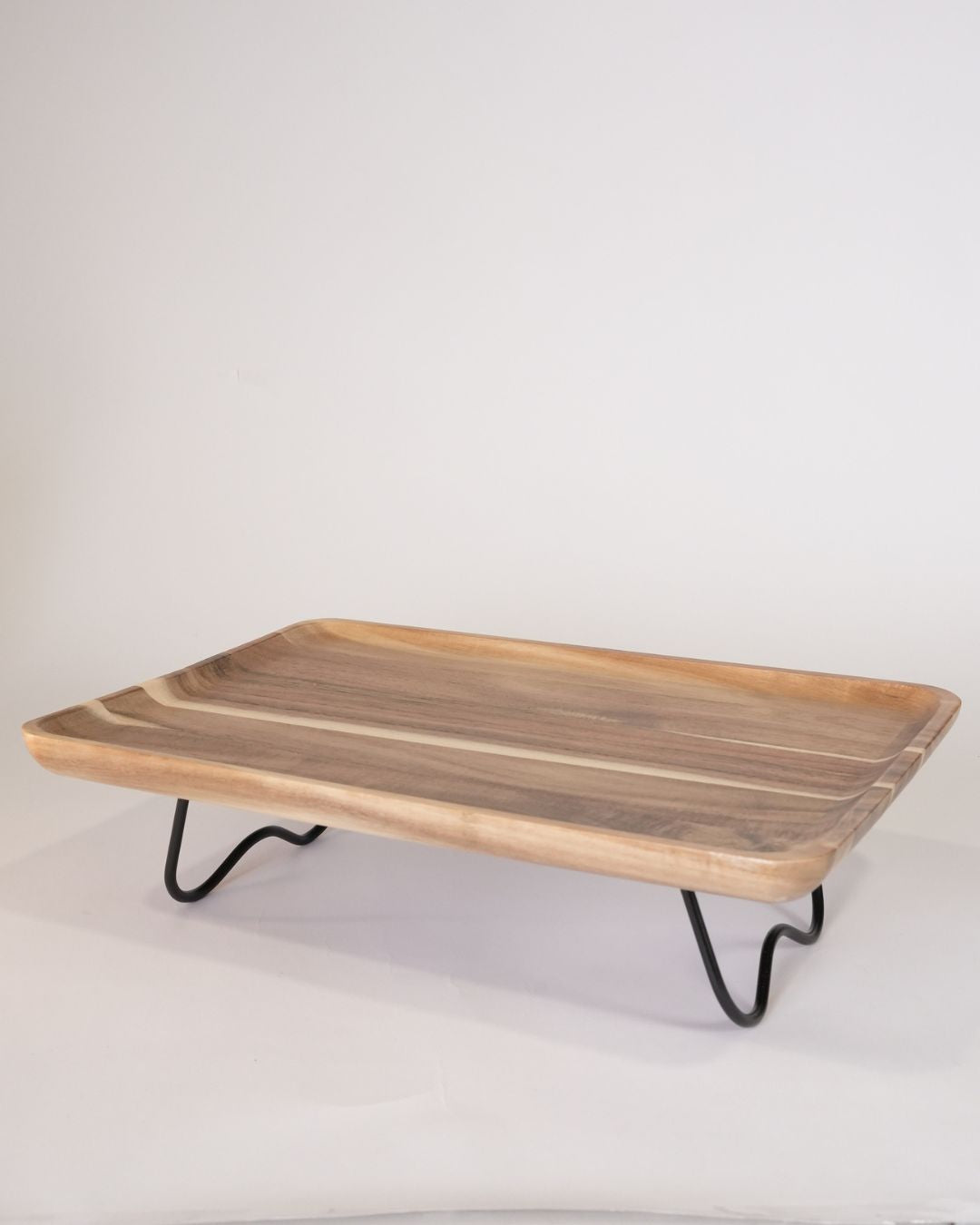 A rectangular wooden serving tray with a live-edge natural wood surface and black metal hairpin legs, Elevated Wood Serving Tray, Raised Wooden Platter with Metal Legs, Wood and Metal Serving Board, Nature Enthusiast Home Decor, Rectangular Wood Table Riser, Solid Hardwood Buffet Platter, Rustic Modern Raised Serving Tray, Black Metal Base Wood Tray, Charcuterie Platter Riser, Biophilic Kitchen Serving Accessories