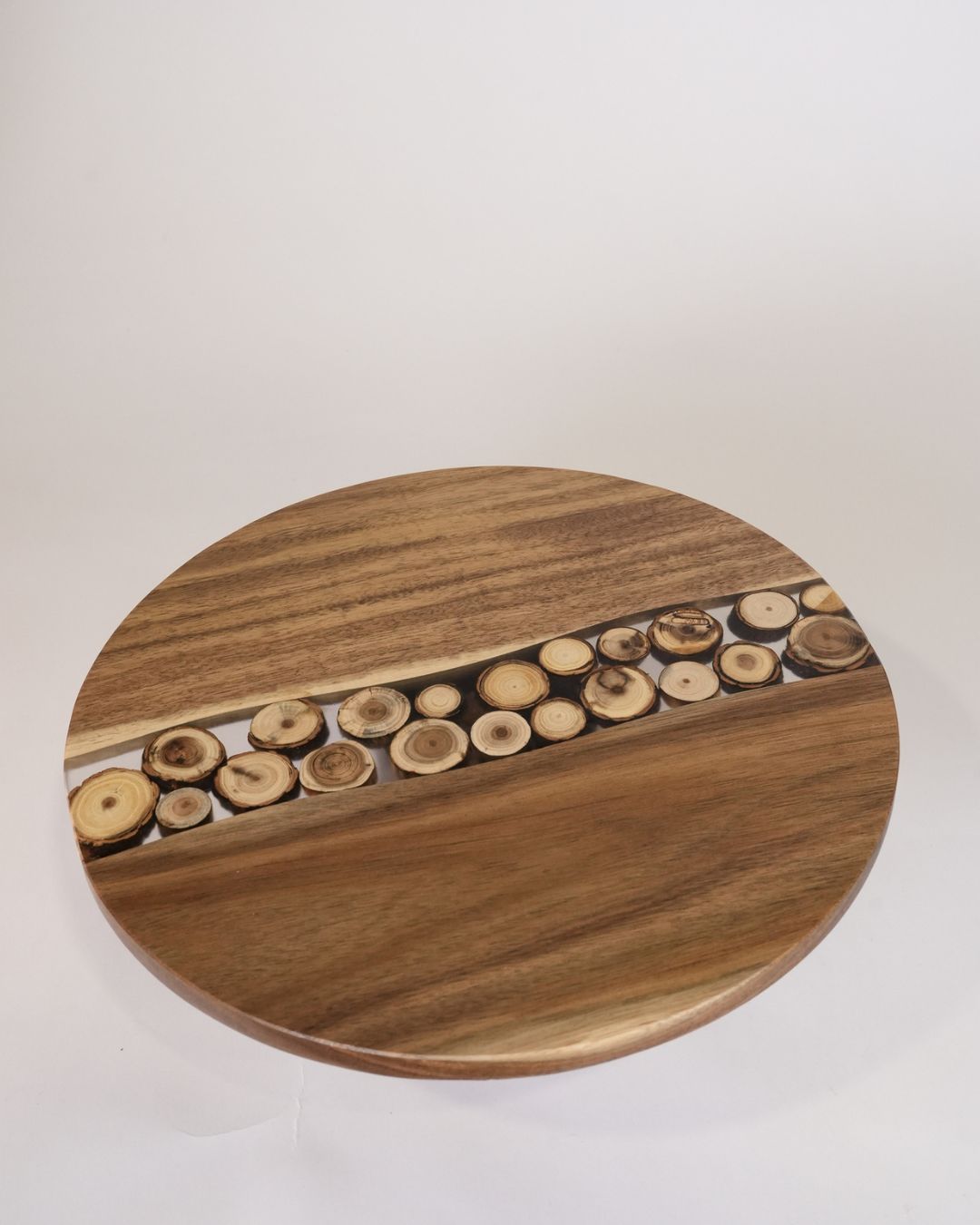 A round wooden serving board or tray with a natural wood grain finish and a central channel filled with small cut wood slices, Wood and Epoxy Resin Cake Stand, Round Wooden Cheese Pedestal, Tree Slice Resin Dessert Riser, Nature Enthusiast Bakery Decor, Handmade Wood Charcuterie Stand, Rustic Modern Cake Platter 12 Inch, Resin River Cake Pedestal, Natural Wood Dessert Buffet Display, Elevated Cheese Board Wood Resin, Biophilic Home Kitchen Accessories