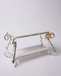 A two-tiered decorative display stand with a polished silver metal frame and white rectangular shelves, accented by gold-toned floral details on the corner supports, set against a plain light gray background.

Silver 2 Tier Serving Stand, Two Tier Ceramic Dessert Stand, High End Catering Dessert Tray, Botanical Bird Food Stand, Rectangular Ceramic Serving Rack, Luxury Party Dessert Display, Silver Metal Tiered Pastry Stand, Upscale Wedding Dessert Tower, Two Tone Buffet Serving Rack, Double Layer Macaron St