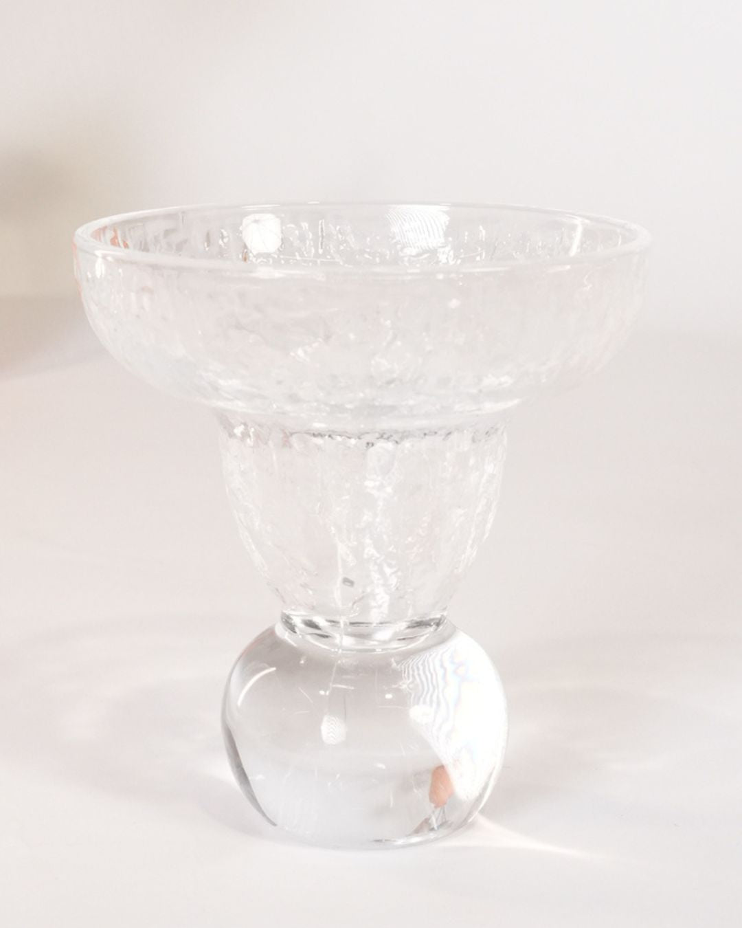 A clear glass pedestal bowl with a textured, hammered finish and a round base, shown on a plain white background.